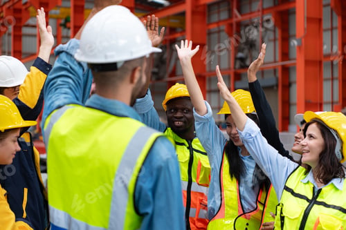 Preview: Group of factory workers in hardhats with arms raised celebrating success