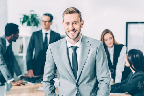 Preview: handsome young manager looking at camera with blurred multicultural businesspeople in conference