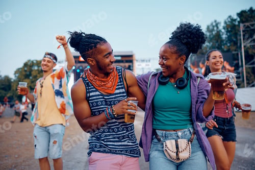 Preview: Cheerful black couple drinking beer and having fun on open air music festival in summer.