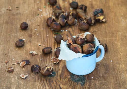 Preview: Roasted chestnuts in blue enamel mug on rustic wooden background, selective focus.