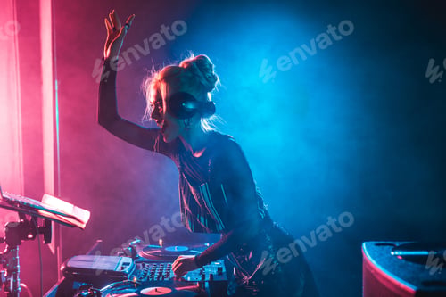 Preview: happy dj girl with blonde hair using dj mixer in nightclub with smoke