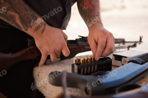 Preview: Tattooed man loading rifle