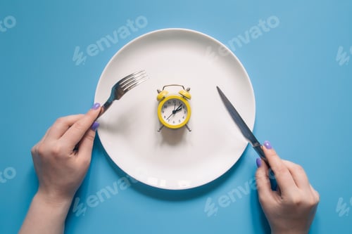 Preview: Hands holding knife and fork above alarm clock on a plate on blue background.