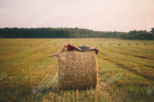 Preview: Beautiful carefree woman lying on haystack enjoying evening in summer field. Atmospheric tranquility