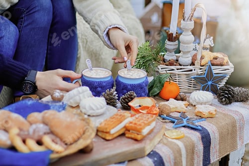 Preview: Hands of a man and a woman hold blue knitted mugs with cocoa and marshmallows. Winter sweet table de