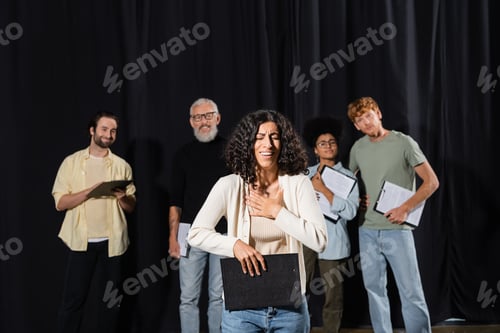 Preview: smiling multiracial woman holding clipboard and smiling near interracial actors and art director on