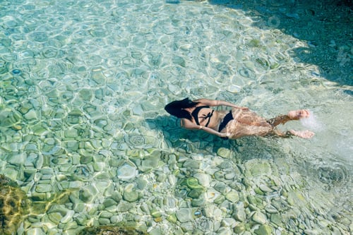 Preview: High angle view of young woman in bikini swimming and diving in transparent turquoise sea water.