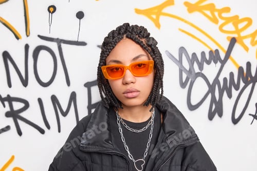 Preview: Photo of serious teenage hipster girl with dreadlocks wears trendy orange sunglasses and black jacke