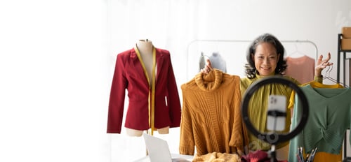 Preview: Happy senior woman doing online clothes business, masuring, holding new beautiful shirt for her cust