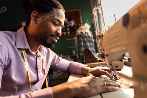 Preview: Male fashion tailor working on the sewing machine for the suit design in his workshop.