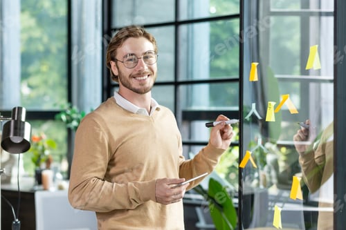 A young designer, programmer, freelancer man is standing in the office, holding a tablet, drawing a