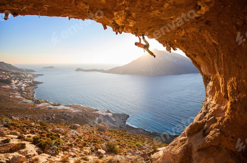 Preview: Male rock climber climbing along a roof in a cave at sunset