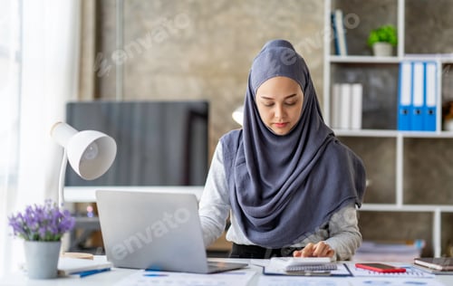 Preview: Attractive Muslim woman wearing a hijab working in a business office Use a calculator and laptop for