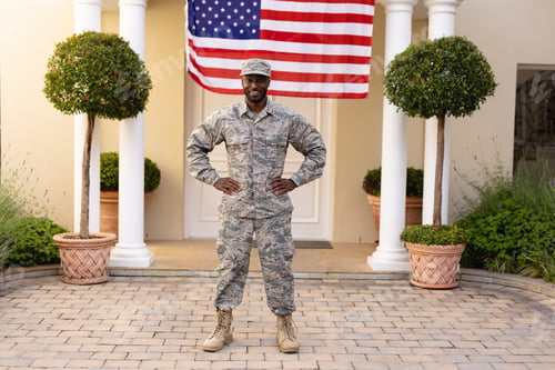 Preview: Portrait of smiling african american army man standing with hand on hip against flag on house