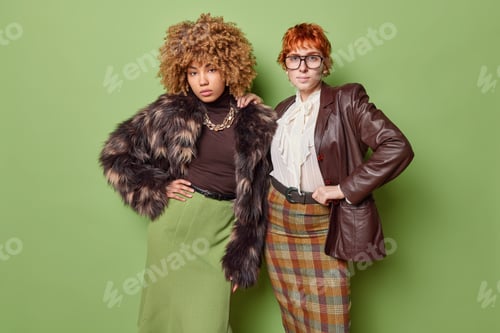 Vista previa: Indoor shot of two fashionable women in blouse shirts and long skirts look confidently at camera