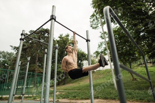 Preview: Young caucasian athlete with muscular torso doing corner on crossbar