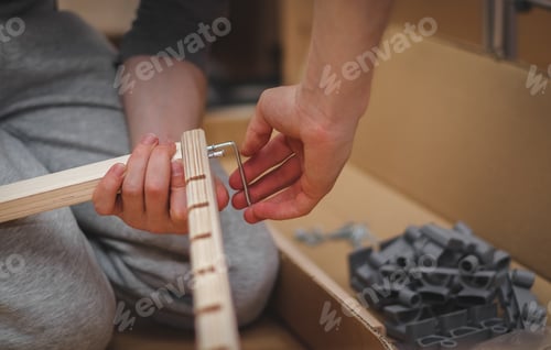 Preview: A man's hands tightening a bolt on a wooden board with a shaped wrench.