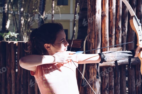 Preview: A young girl practicing archery, aiming at a target with a bow and arrow