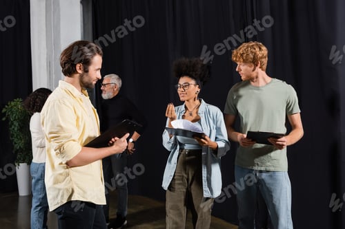 Preview: smiling african american woman with scenario talking to young actors in acting skills school