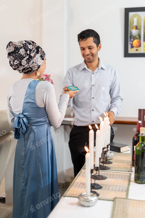 Preview: Jewish woman giving hanukkah cookie to her husband during dinner. Hanukkah celebration concept.