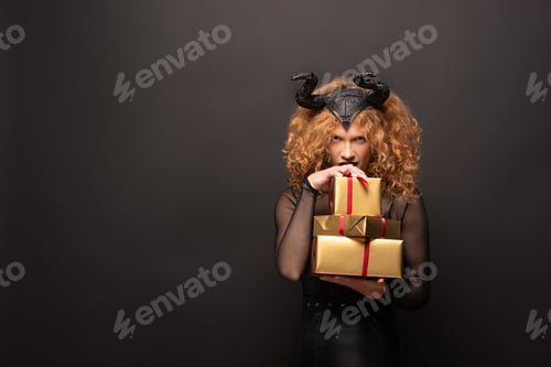 Preview: scary woman in maleficent costume holding gift boxes for halloween on black