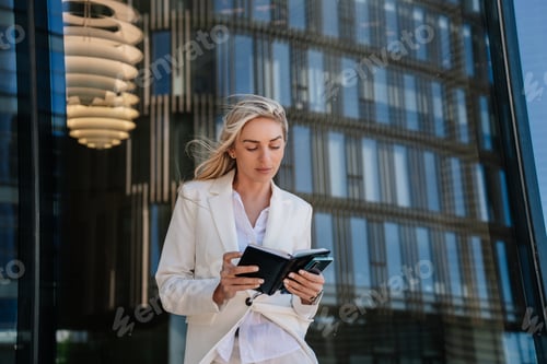 Preview: Purposeful caucasian young woman in white suit with fluttering hair, holds diary focused on agenda
