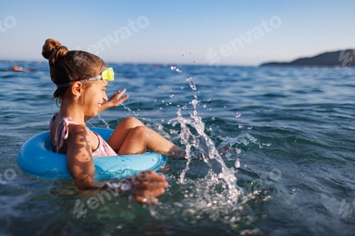 Preview: Cheerful girl sits in an inflatable circle and splashes with water in the sea