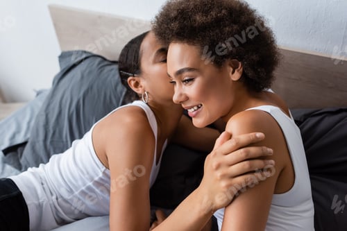 Preview: african american lesbian woman kissing cheek of happy girlfriend in bedroom