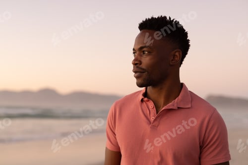 Preview: Thoughtful african american handsome young man standing at beach against clear sky during sunset