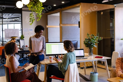 Preview: Diverse female colleagues in discussion using tablet in casual office meeting