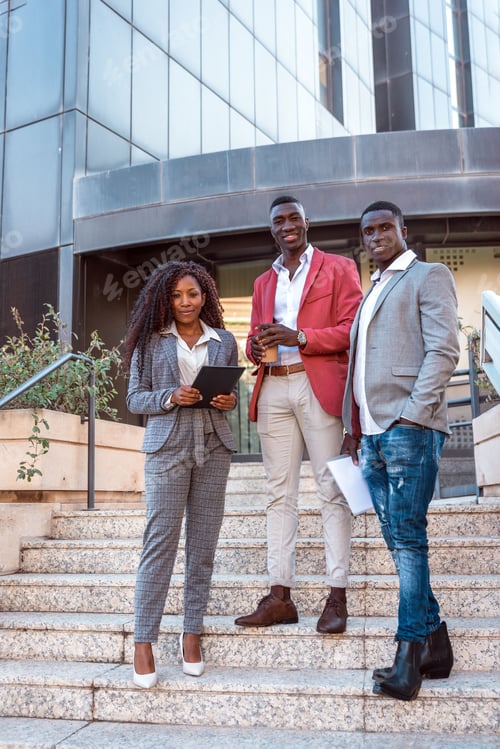 Preview: Multiracial diverse business team standing on stairs in front of office building smiling at camera