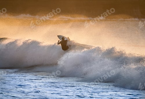 Preview: A surfer on a wave at dawn with golden light shiny through the ocean spray