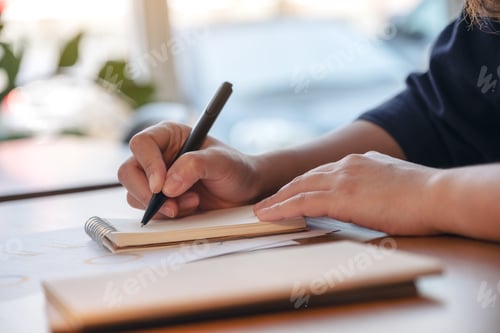 Preview: Closeup image of a hand writing on blank notebook on wooden table