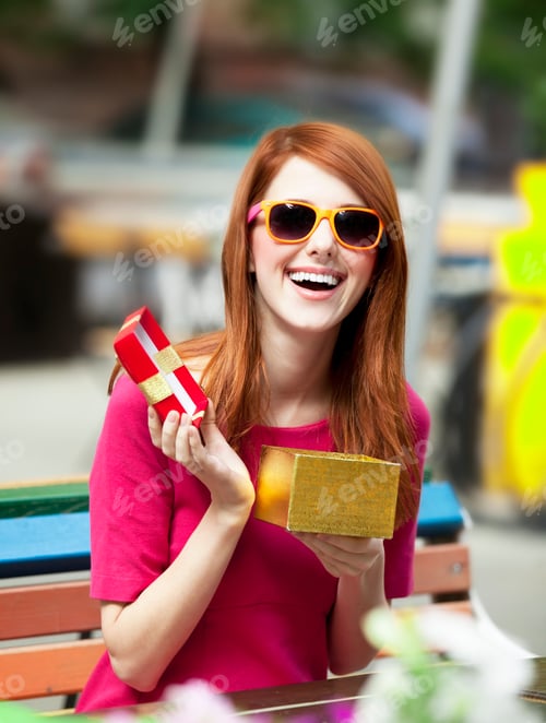 Preview: Style redhead girl with gift sitting on the bench in the cafe