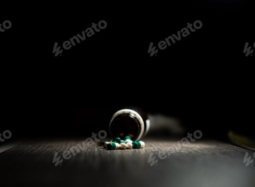 Preview: Closeup shot of white-green capsule pills spread out of a glass drug bottle on black background