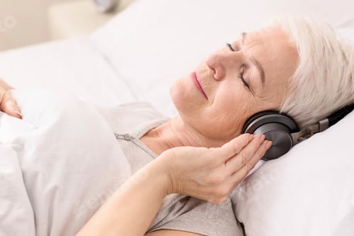 Preview: Old Woman Laying in Bed With Headphones On
