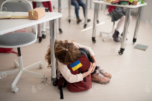 Preview: Little sad Ukrainian girl sitting on floor at school, concept of enrolling Ukrainian kids to schools