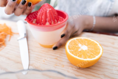 Preview: Close up of a young Hispanic woman is squeezing an orange to make orange and carrot juice outdoors
