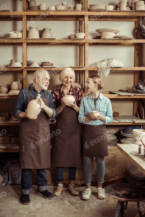 Preview: Granddaughter and grandparents standing and holding clay vase and bowls against wall with pottery