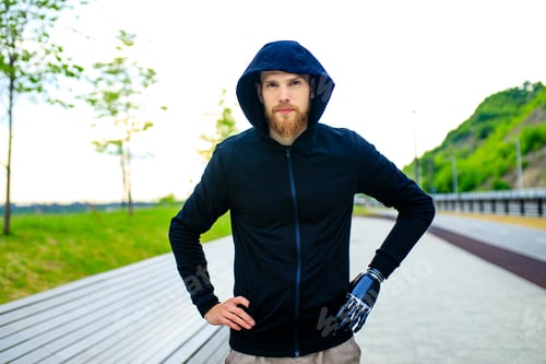 Preview: man with arm prosthesis in sports clothing ready for morning workout outdoors.