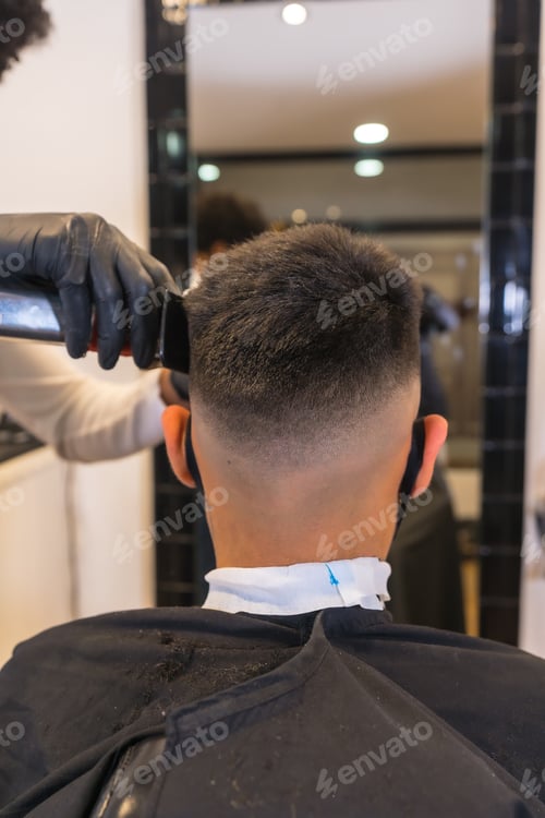 Preview: Hairdresser with mask and gloves cutting the hair of the young client.