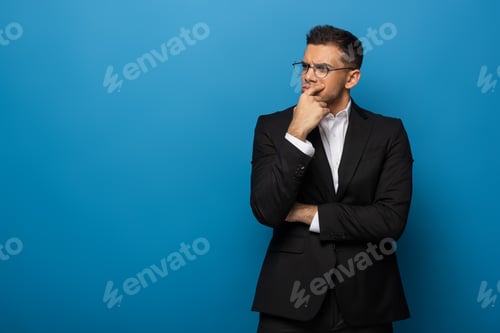 Preview: Thoughtful businessman with hand by chin looking away on blue background