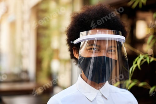 Preview: Happy black waitress with visor and protective face mask at outdoor cafe.