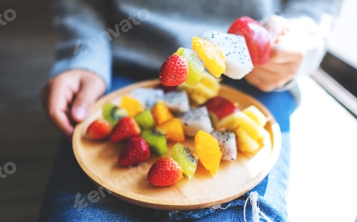 Preview: Closeup image of a woman holding a wooden plate of fresh mixed fruits on skewers