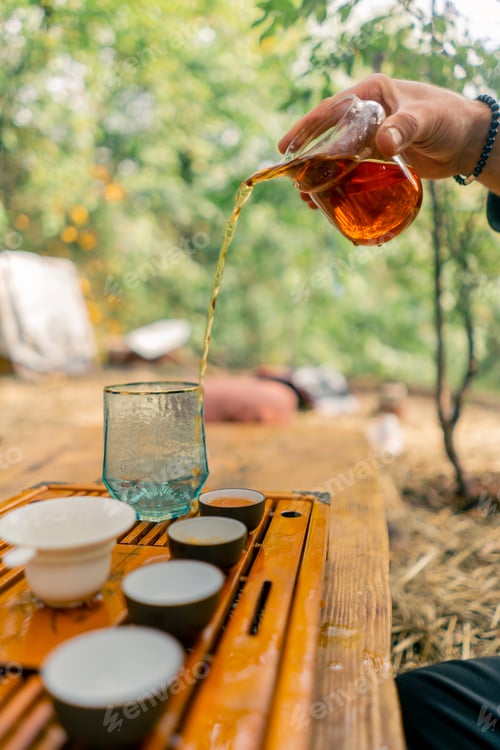 Preview: Close-up shot of a man's hand pouring brewed natural tea into ceramic bowls lined up in row