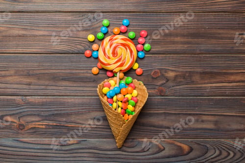 Preview: waffle cone full of assorted traditional candies falling out on colored background