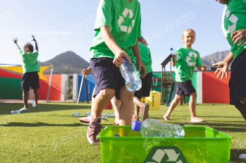 Preview: Low angle view of multi ethnic students putting plastic bottles on dustbin in schoolyard