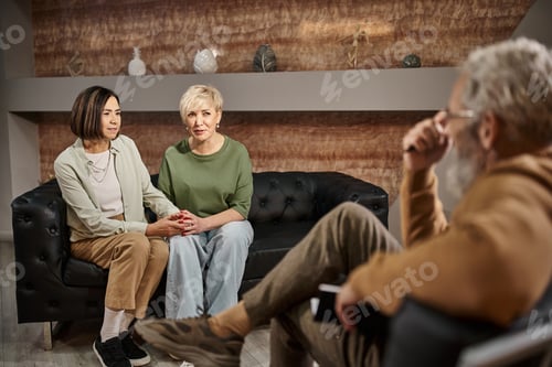 Preview: middle aged lesbian couple talking and sitting on couch near psychologist during session