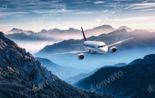 Preview: Airplane is flying over mountains in fog at colorful sunset