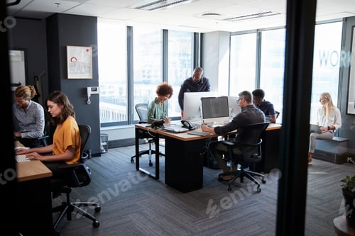 Visualização: Jovem equipe criativa trabalhando em conjunto em computadores em um escritório casual, vista da porta